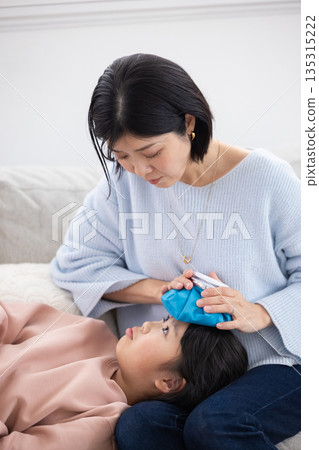 Mother applying ice pack to daughter's forehead Mother applying ice pack to daughter's forehead 135315222