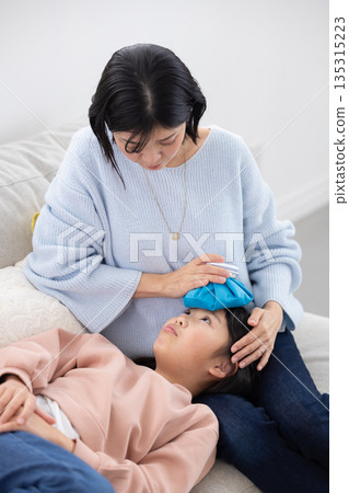 Mother applying ice pack to daughter's forehead 135315223