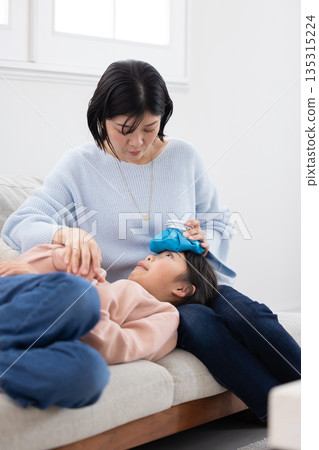Mother applying ice pack to daughter's forehead Mother applying ice pack to daughter's forehead 135315224