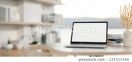 White screen laptop with books and rice spike in vase on table in a living room with outside scenery White screen laptop with books and rice spike in vase on table in a living room with outside scenery 135315348