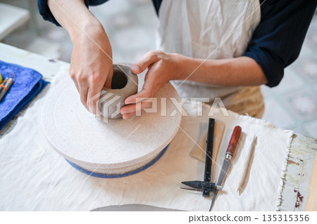 Close up potter artist molding clay to make mug cup on working table in pottery studio or classroom. Close up potter artist molding clay to make mug cup on working table in pottery studio or classroom. 135315356