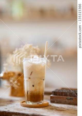 A glass of iced milk tea or coffee aside wooden blocks on working table in a pottery studio or cafe. 135315366