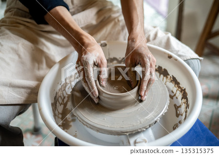 Close up of pottery artist's hands making a clay bowl on spinning throwing wheel in class or studio. Close up of pottery artist's hands making a clay bowl on spinning throwing wheel in class or studio. 135315375