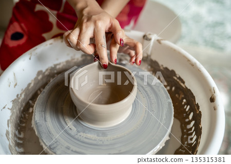 Pottery artist hand molding clay into tea brewing bowl on spinning throwing wheel in class or studio Pottery artist hand molding clay into tea brewing bowl on spinning throwing wheel in class or studio 135315381