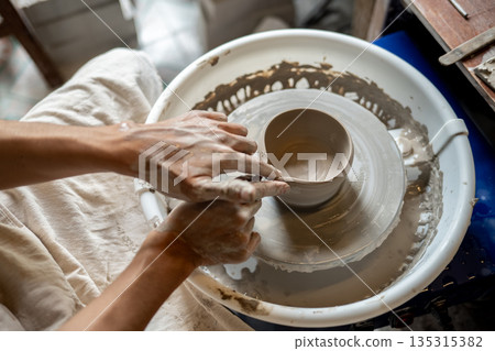 Pottery artist hand making clay into tea brewing bowl on spinning throwing wheel in class or studio. 135315382