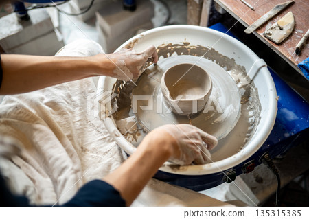 Pottery artist finish making a clay tea brewing bowl on spinning throwing wheel in class or studio. Pottery artist finish making a clay tea brewing bowl on spinning throwing wheel in class or studio. 135315385