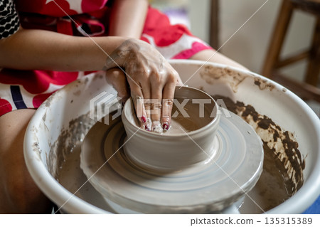 Painted nails pottery artist molding clay into a bowl on spinning throwing wheel in class or studio. Painted nails pottery artist molding clay into a bowl on spinning throwing wheel in class or studio. 135315389