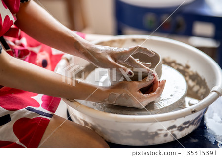 Painted nail pottery artist molding pour spout tea brewing bowl on throwing wheel in class or studio Painted nail pottery artist molding pour spout tea brewing bowl on throwing wheel in class or studio 135315391