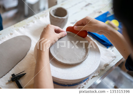 Pottery artist using a throwing tool on clay to make a circle at working table in a class or studio. 135315396