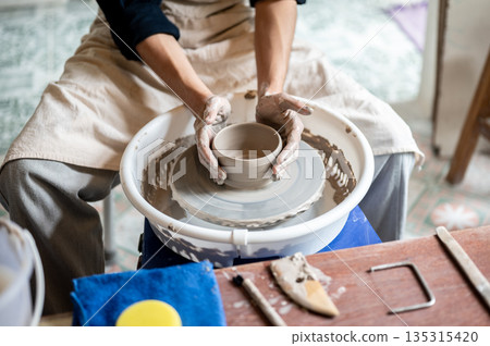 Close up pottery artist's hands molding smooth clay bowl or cup on throwing wheel in class or studio Close up pottery artist's hands molding smooth clay bowl or cup on throwing wheel in class or studio 135315420