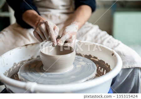 Close up pottery artist making pour spout on clay brewing bowl on throwing wheel in class or studio. Close up pottery artist making pour spout on clay brewing bowl on throwing wheel in class or studio. 135315424
