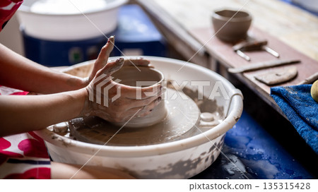 Close up painted nails woman pottery artist molding a clay bowl on throwing wheel in class or studio Close up painted nails woman pottery artist molding a clay bowl on throwing wheel in class or studio 135315428