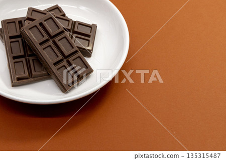 Brown background and a chocolate bar on a plate Brown background and a chocolate bar on a plate 135315487