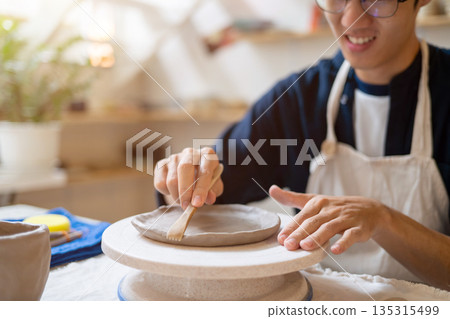 Potter artist glasses man molding clay to make a plate on working table in a pottery class or studio. 135315499