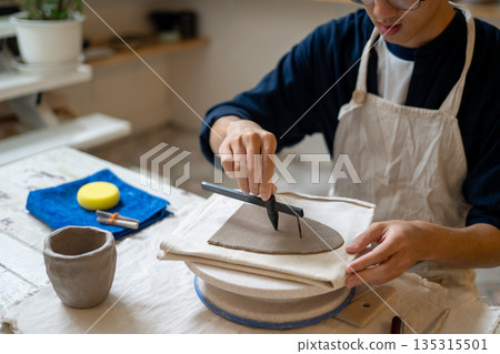 Glasses man potter artist cutting molding clay slab on working table in pottery class or studio room 135315501