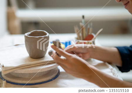 Potter artist holding and adding a handle to mug cup on working table in a pottery class or studio. 135315510