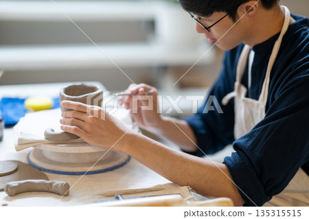 Potter artist holding brush adding texture on clay mug on working table in a pottery class or studio 135315515