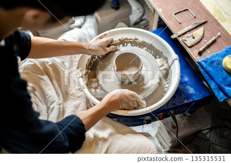 Close up pottery artist look at clay tea brewing bowl on spinning throwing wheel in class or studio 135315531