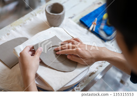 Pottery artist taking out circle clay from slab on throwing wheel at work table in a class or studio Pottery artist taking out circle clay from slab on throwing wheel at work table in a class or studio 135315553