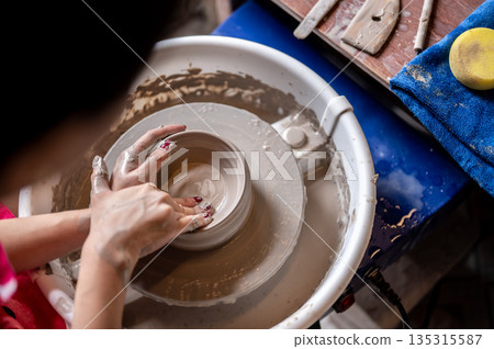 Red painted nails woman pottery artist molding a clay bowl on spin throwing wheel in class or studio 135315587