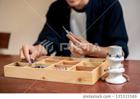 Young man artist choosing ceramic beads to make colorful bracelet from wooden box in class or studio Young man artist choosing ceramic beads to make colorful bracelet from wooden box in class or studio 135315589