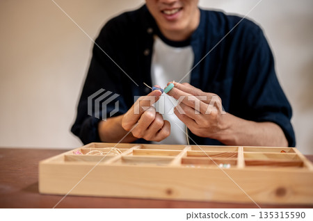 Young man choosing ceramic beads on thread from wooden box while making a bracelet in class or studio Young man choosing ceramic beads on thread from wooden box while making a bracelet in class or studio 135315590
