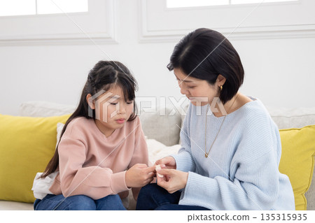 A mother putting a bandage on her elementary school daughter's finger A mother putting a bandage on her elementary school daughter's finger 135315935