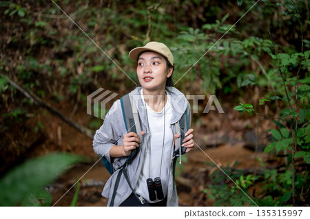 Asian woman tourist walking holding bag straps and looking around during forest hiking or trekking. 135315997