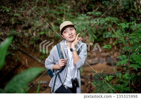 Pretty asian woman tourist walking holding bag strap wiping sweat during forest hiking or trekking. 135315998