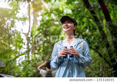Pretty asian woman tourist smiling as holding binoculars while hiking or trekking in mountain forest 135316035