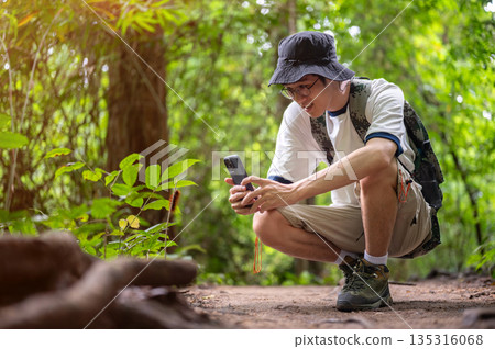 Man tourist crouching taking picture of a plant or animal on phone during forest hiking or trekking. 135316068