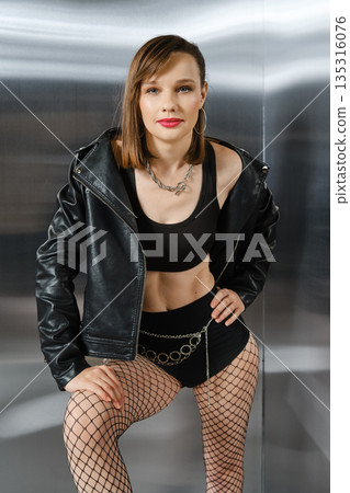 Woman poses confidently in black outfit near shiny silver backdrop during photo shoot Woman poses confidently in black outfit near shiny silver backdrop during photo shoot 135316076