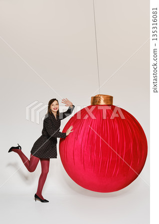 Woman poses with large red ornament during festive studio session for holiday celebration Woman poses with large red ornament during festive studio session for holiday celebration 135316081