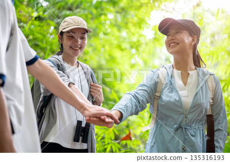 Backpacker tourist group of man and woman friends joining hands while hiking or trekking in a forest 135316193