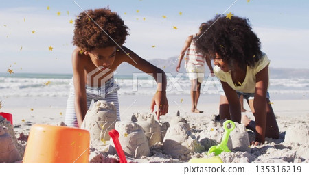 Kids shaping sandcastles on beach, father walking behind, with orange bucket, red and green shovels Kids shaping sandcastles on beach, father walking behind, with orange bucket, red and green shovels 135316219