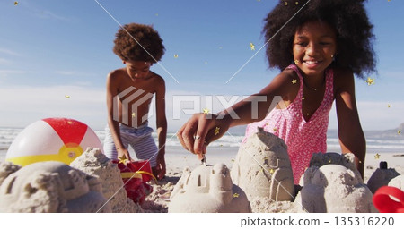 School-age siblings in swimwear building sandcastles at beach, with red buckets shovel beach ball School-age siblings in swimwear building sandcastles at beach, with red buckets shovel beach ball 135316220