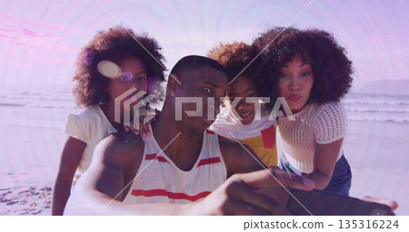 Taking family of four selfie capturing ocean view at beach, with striped tank top and smartphone 135316224