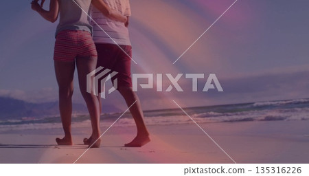 Walking couple in casual beachwear barefoot along wet sand on beach, with ocean waves and coastline Walking couple in casual beachwear barefoot along wet sand on beach, with ocean waves and coastline 135316226
