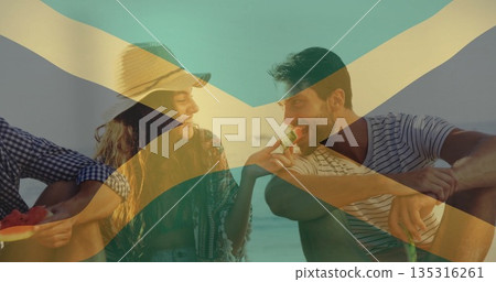 Sharing watermelon slices friends wearing straw sunhat cover-up and striped t-shirt at sandy beach 135316261