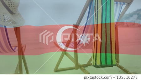 Wooden folding chairs facing sea on beach with pastel-striped seats, striped towel, straw sun-hat 135316275