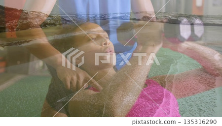 Trainer spotter supporting man lifting hexagonal dumbbells on bench at gym, with ocean wave overlay 135316290