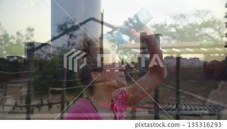 Drinking woman wearing pink workout top raising clear blue bottle on balcony, with city skyline Drinking woman wearing pink workout top raising clear blue bottle on balcony, with city skyline 135316293