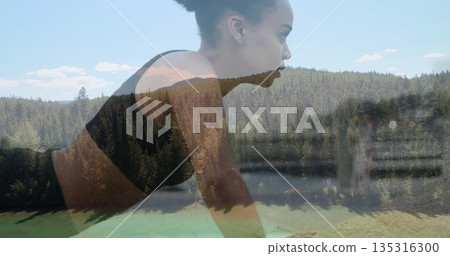 Holding plank woman wearing dark sports bra and leggings at forested lakeshore, with exercise mat Holding plank woman wearing dark sports bra and leggings at forested lakeshore, with exercise mat 135316300