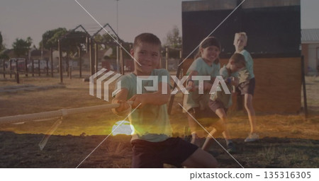 Pulling group of four boys tugging thick rope on playground grass, with wooden obstacle wall 135316305