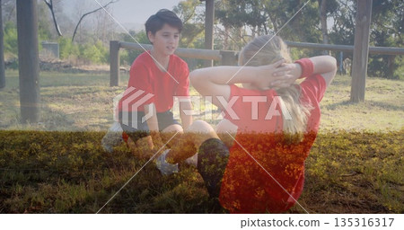 Performing sit-ups kids wearing red sports shirts at grassy park, with wooden posts and beams 135316317