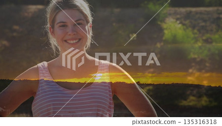 Smiling woman wearing pink striped tank top posing hands on hips at clearing, golden light band Smiling woman wearing pink striped tank top posing hands on hips at clearing, golden light band 135316318