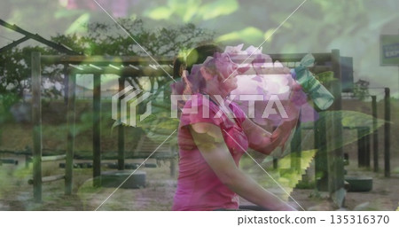 Woman in pink shirt drinking from green water bottle at obstacle course, with frames, beams, tires Woman in pink shirt drinking from green water bottle at obstacle course, with frames, beams, tires 135316370