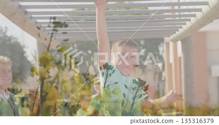 Boy swinging from monkey bars in playground, with coach wearing whistle lanyard, foliage, columns 135316379
