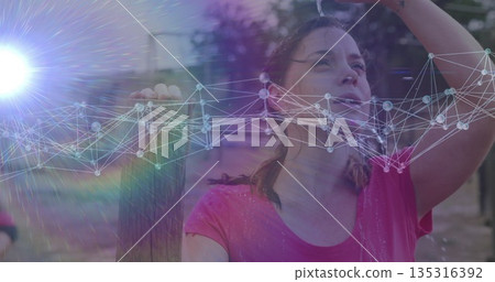 Leaning woman in pink shirt raising hand above head at park, with fence and water droplets Leaning woman in pink shirt raising hand above head at park, with fence and water droplets 135316392