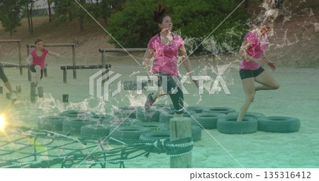 Jumping woman wearing pink top and black leggings on park course, with tires and rope net 135316412